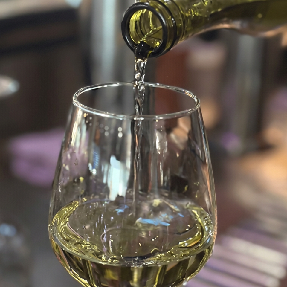 White wine pours from a bottle into a stemless glass at a softly lit restaurant table.